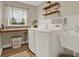 Modern laundry room with wooden shelves, a built-in desk, stainless steel sink and modern white appliances at 6321 Clearmeadow Ct, Windermere, FL 34786