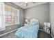 Well-lit bedroom featuring a large window, ceiling fan, and cozy blue bedding, complemented by neutral gray walls at 17516 Blessing Dr, Clermont, FL 34714