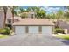 Garage with a black paved driveway, beige facade, three doors and lush trees at 2142 Woodbridge Rd, Longwood, FL 32779