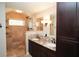 Bathroom featuring double sinks, granite countertops, walk-in shower with tan tiling and dark wood cabinets at 687 N Endeavour Dr, Winter Springs, FL 32708