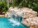 Close up of a gorgeous rock waterfall cascading into a sparkling pool with tropical foliage surrounding it at 11106 Coniston Way, Windermere, FL 34786