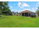 Spacious backyard showcasing lush green grass, mature trees, a screened-in patio, and manicured landscaping at 23538 Valderama Ln, Sorrento, FL 32776