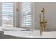 Modern bathroom with a standalone tub, brass fixtures, and a window with plantation shutters at 23538 Valderama Ln, Sorrento, FL 32776