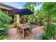 Back patio features a dining table, umbrella, paver stones, mature tropical trees, and lush landscaping at 489 Grape Ave, St Cloud, FL 34769