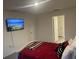 Bright bedroom with a red bedspread, wall-mounted TV, and view into the hallway at 7172 Sw 135Th Pl, Ocala, FL 34473