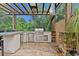 A covered outdoor kitchen equipped with a grill, refrigerator, and counter space, set in a stone-paved area with lush greenery at 4048 Gilder Rose Pl, Winter Park, FL 32792