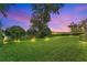 Backyard featuring lush green grass, mature trees, and an elegant black fence at dusk at 1938 Filly Trl, Oviedo, FL 32765