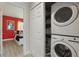 Bright laundry area featuring a stacked washer and dryer and an adjacent bedroom painted with a bold red accent wall at 2531 Maneshaw Ln, Kissimmee, FL 34747