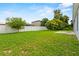 Large grassy backyard featuring a white fence, lush trees, and a concrete patio area at 446 Arkansas Ct, Poinciana, FL 34759