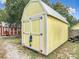 A yellow storage shed with white trim on a level foundation presents a secure space for tools and outdoor equipment in a well-maintained yard at 219 E Fern Dr, Orange City, FL 32763