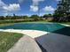 Swimming pool with green safety cover surrounded by concrete, grass, trees, and overhead powerlines in a sunny backyard at 4534 Lemans Dr, Orlando, FL 32808