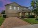 Charming two-story home featuring a brick driveway and manicured front lawn with lush greenery at dusk at 2432 Riviera Ln, Minneola, FL 34715