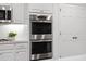 Close-up shot of the kitchen's stainless steel double ovens, white cabinetry, and tiled backsplash at 2432 Riviera Ln, Minneola, FL 34715