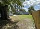Backyard with a lawn, a shed, a wood fence, and mature trees under a sunny sky with fluffy white clouds at 910 Flamingo Dr, Leesburg, FL 34748