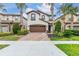 Beautiful two-story home featuring a brown garage door, brick driveway, and lush landscaping, with palm trees at 8912 Rhodes St, Kissimmee, FL 34747