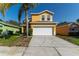 Two-story yellow home featuring a two-car garage and a well-maintained front yard with a mature palm tree at 1129 Royal Ridge Dr, Davenport, FL 33896