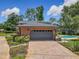 View of a brick garage with a dark gray door, paver driveway and fenced backyard pool at 1850 Lakeshore Cir, Longwood, FL 32750