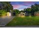 Beautiful home exterior at dusk with lush green lawn, long driveway, and tasteful landscaping with tropical plants at 6805 Barby Ln, Belle Isle, FL 32812