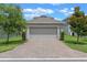 View of the two-car garage with brick paver driveway and green lawn and landscaping at 1378 Roxy Ln, Winter Garden, FL 34787