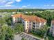 Exterior shot of a multi-story condo building with a red tile roof surrounded by green trees and a parking lot at 8020 Tuscany Way # 6301, Davenport, FL 33896