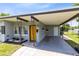 View of a convenient covered carport with a yellow front door and gray siding, and manicured landscaping at 3515 Leslie Dr, Orlando, FL 32806