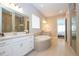 A bright bathroom featuring double vanities, a soaking tub, a tiled shower stall with glass door and tile floors at 7388 John Hancock Dr, Winter Garden, FL 34787