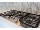 Close-up view of a stainless steel gas cooktop with stylish backsplash and white quartz countertops at 7388 John Hancock Dr, Winter Garden, FL 34787