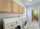 Well-lit laundry room with a front-load washer, dryer, and upper wooden cabinets at 9454 Candice Ct, Orlando, FL 32832