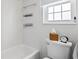 Bright bathroom featuring a white toilet, tub, and tiled walls, complemented by mounted storage and a window at 1100 E Caroline St # 204, Tavares, FL 32778