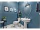 Stylish powder room with a pedestal sink, blue walls, decorative mirror, and modern lighting at 17676 Passionflower Cir, Clermont, FL 34714