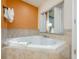 Bathroom featuring a jetted bathtub with beige tile surround, an orange accent wall and a window to the bedroom at 12527 Floridays Resort Dr # E104, Orlando, FL 32821