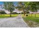 Long gravel driveway leading to a property with grassy fields and mature trees on either side at 16610 County Line Rd, Umatilla, FL 32784
