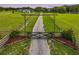 Long driveway with an iron gate and a rustic wooden structure surrounded by green fields at 16610 County Line Rd, Umatilla, FL 32784