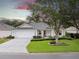 Charming one-story home with a manicured lawn, mature trees, and a two-car garage against a colorful sky at 16950 Se 80Th Bellavista Cir, The Villages, FL 32162