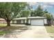 Traditional single-story home with white siding, gray trim, and a two-car garage, accented by mature trees at 9551 Lake Douglas Pl, Orlando, FL 32817