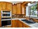 A kitchen area with stainless steel ovens, wooden cabinets, tile countertops, and a black double sink under a window at 205 Trail Bridge Ct, Winter Garden, FL 34787