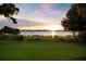 Breathtaking sunset lake view from a grassy shoreline with natural reeds and mature trees at the edges of the frame at 15787 Tangerine Dream Ct, Winter Garden, FL 34787