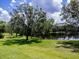 Scenic view of a lush green lawn sloping to a pond, framed by mature shade trees under a partly cloudy sky at 1941 Sunset Palm Dr, Apopka, FL 32712