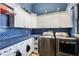 Modern laundry room with blue backsplash, white cabinets, and stainless steel washer and dryer units at 5413 Via Veneto Ct, Sanford, FL 32771