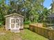 An outside shed with double doors, nestled in a backyard with a wooden fence, grass, and mature trees at 5489 Glen Oak Place, Sanford, FL 32771