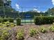 Community tennis court with a bright blue surface, green fence, and landscaping at 164 Royal Palm Dr, Leesburg, FL 34748