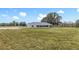 Scenic rear exterior with a vast green lawn and distant trees under a partly cloudy sky at 14243 County Road 450, Umatilla, FL 32784