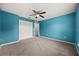 Vibrant blue bedroom featuring plush carpet, a ceiling fan, and double closets for ample storage at 2725 White Magnolia Loop, Clermont, FL 34711