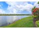 Picturesque view of a calm pond with a grass shoreline and flowering trees under a bright sky at 2440 Pawtucket Pass, Mount Dora, FL 32757