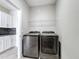 Bright laundry room featuring modern gray washer and dryer units, complemented by overhead storage shelving at 1556 Alligator St, St Cloud, FL 34771