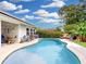 Backyard pool is surrounded by patio seating and lush landscaping under a cloudy blue sky at 14529 Falling Tree Ct, Orlando, FL 32837