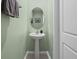 Stylish powder room with a pedestal sink, oval mirror, and soft green walls at 253 Fiddlewood Ct, Davenport, FL 33837