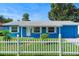 Charming blue single-story home featuring a white picket fence, green lawn, and blue sky at 4654 Alhama St, Orlando, FL 32811