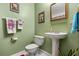 Bathroom featuring a pedestal sink, toilet, and green walls with framed artwork at 5324 Barefoot Path, Kissimmee, FL 34746