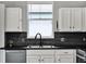 Close-up of the kitchen sink with black hardware, white cabinets, stainless steel dishwasher, and black backsplash at 1712 Riveredge Rd, Oviedo, FL 32766